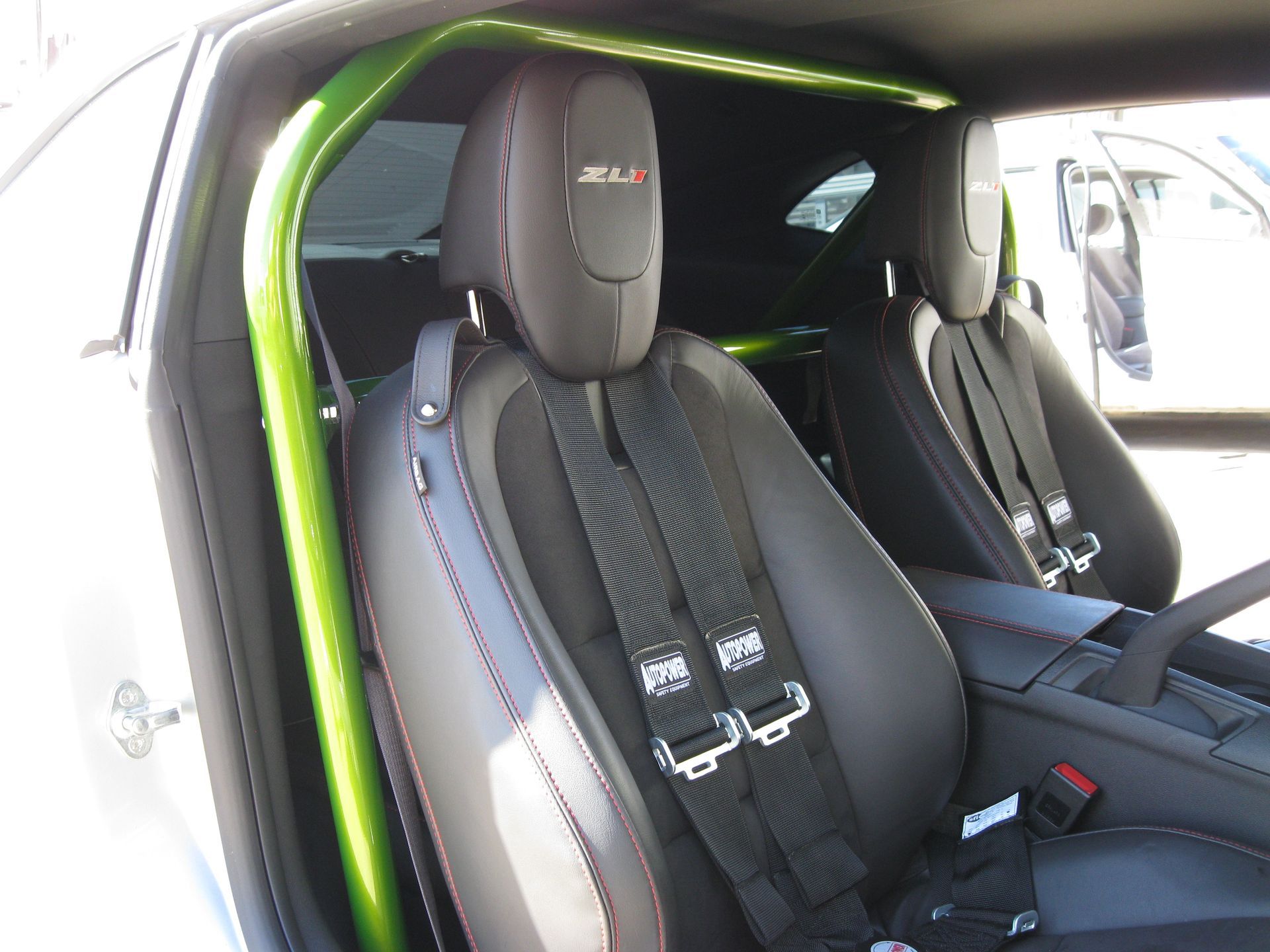 Interior of a car with black racing seats, green roll cage, and black safety harnesses.