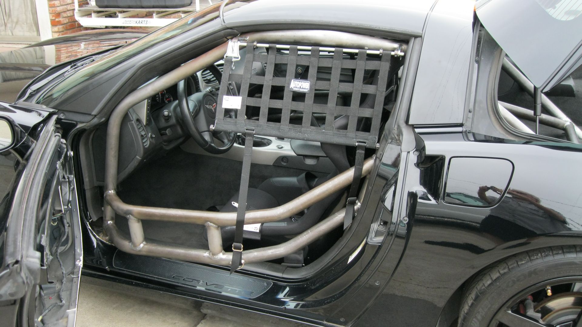 Black Corvette with roll cage, safety net, and open door.