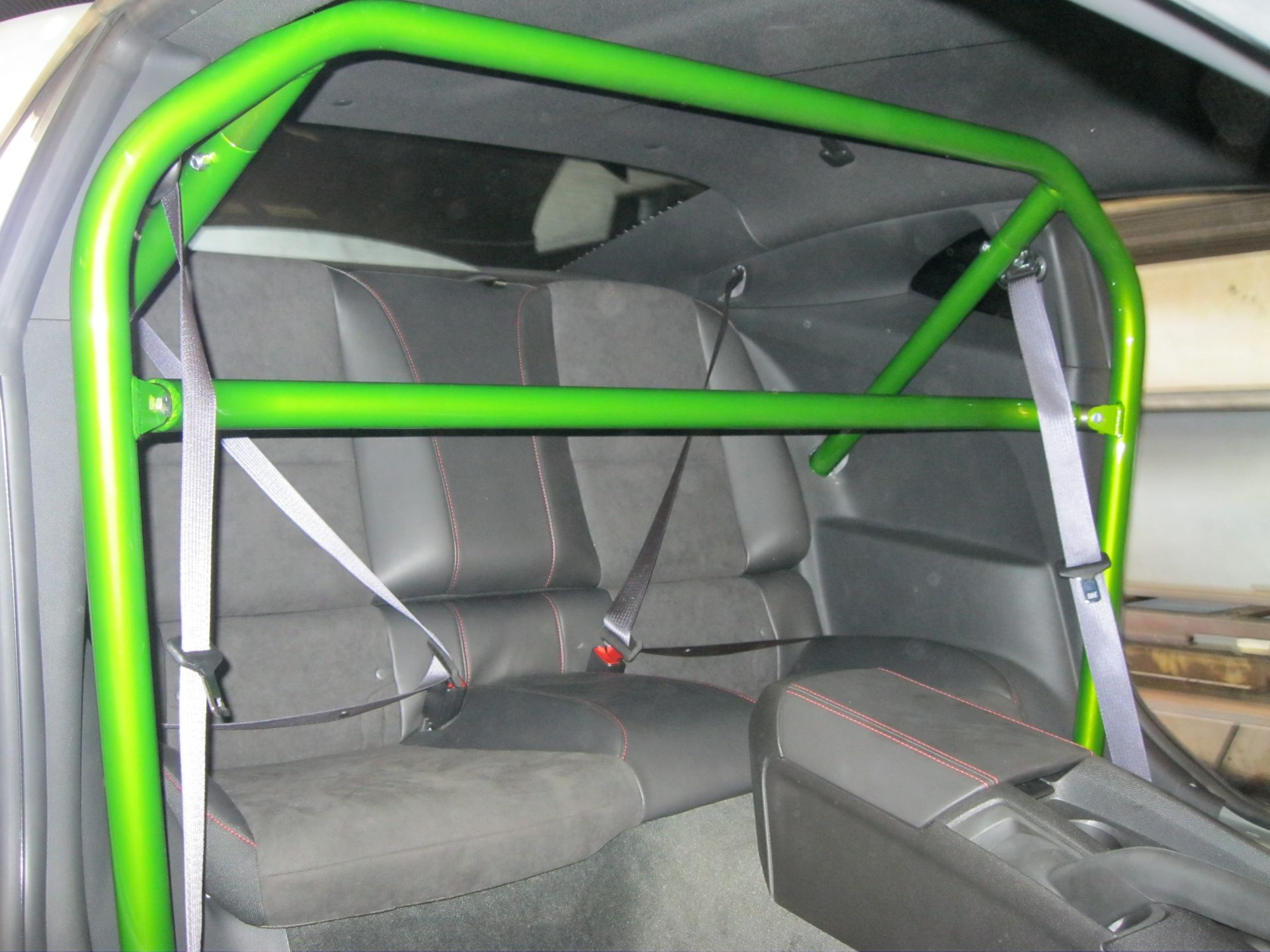 Green roll cage installed inside a car, with rear seats and seatbelts visible.