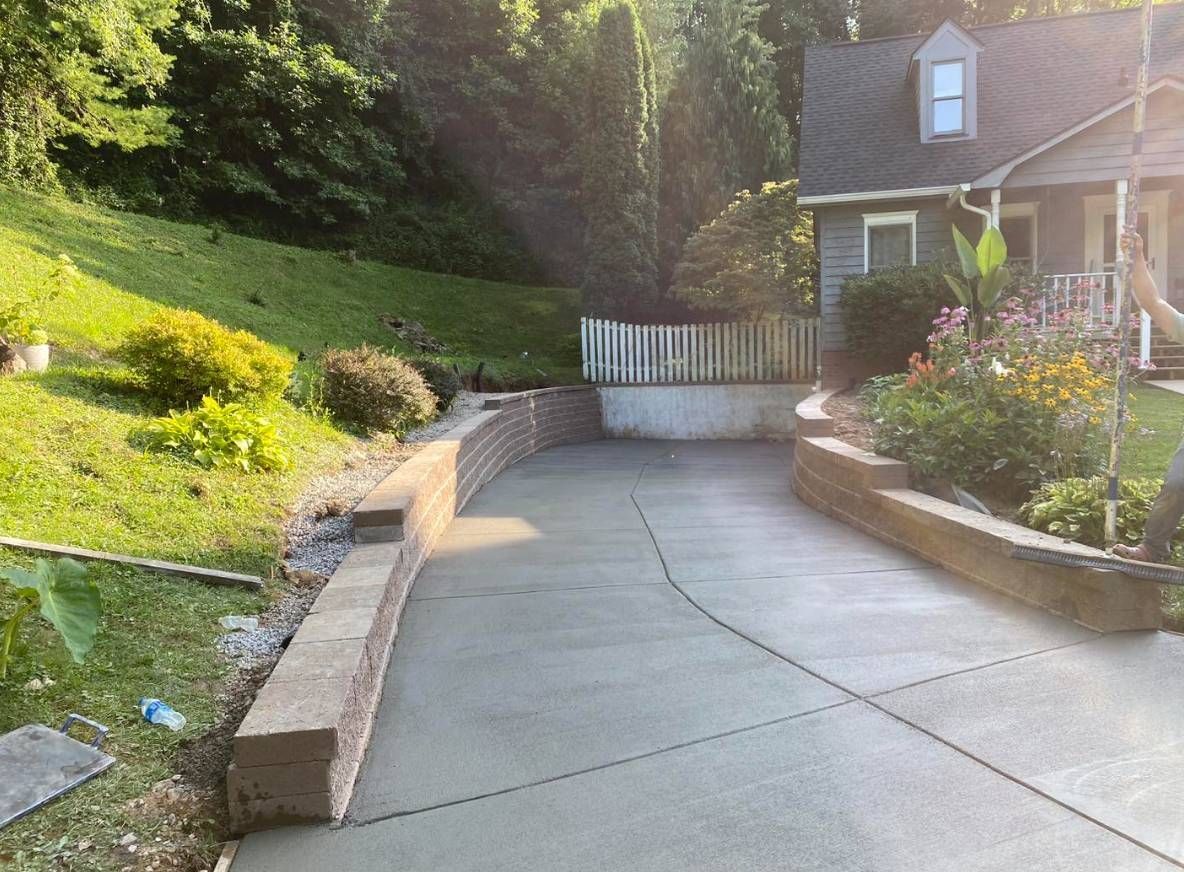 A concrete driveway leading to a house in the woods.