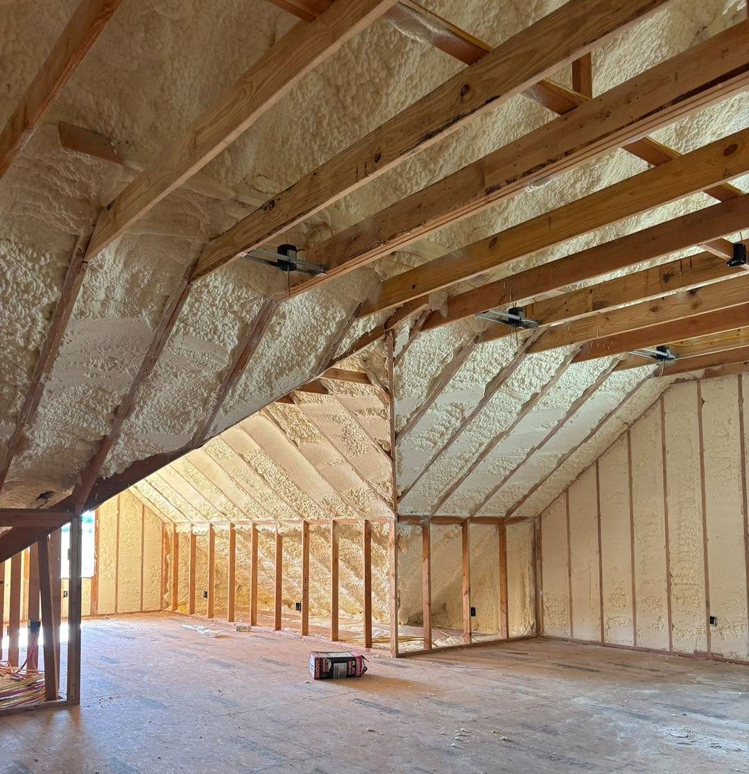 Insulated attic interior with exposed wooden rafters and spray foam on the roof and walls
