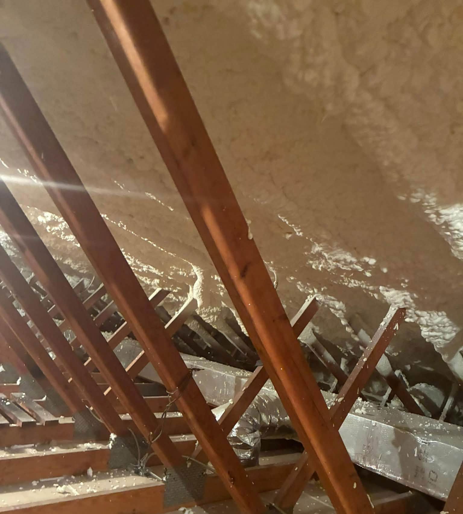 Damaged attic roof with exposed wooden beams and rubble scattered across the insulation.