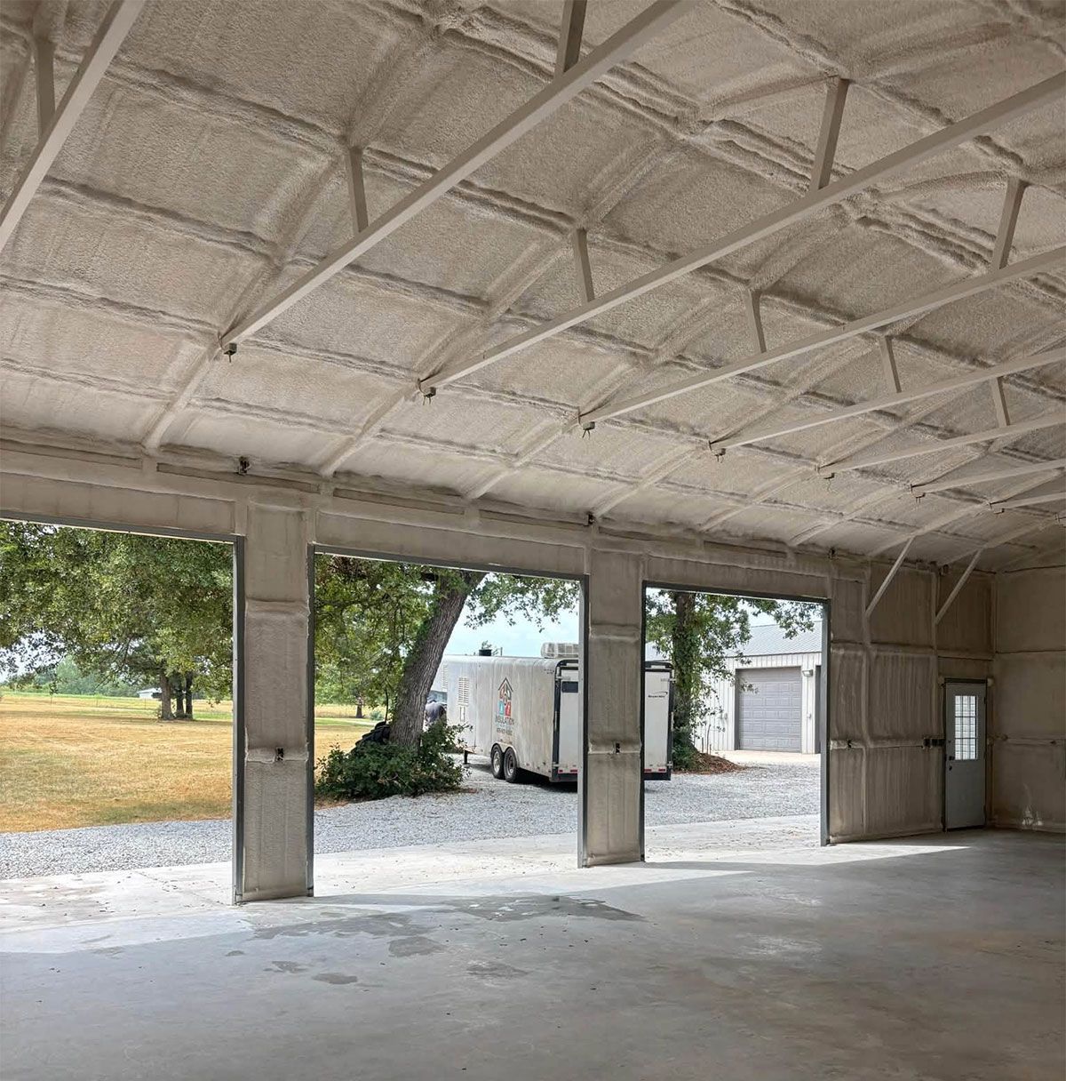 Empty unfinished garage with concrete floor, open bay openings, and white insulated ceiling panels.