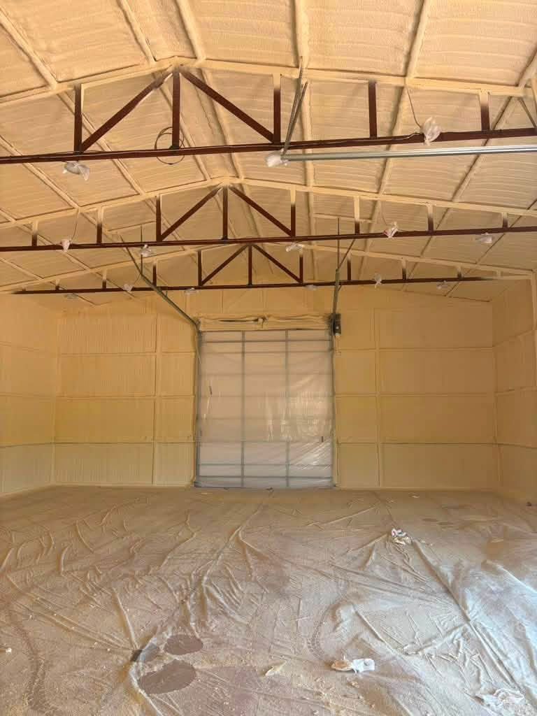 Empty beige warehouse interior with exposed ceiling trusses and a closed roll-up door at the back.
