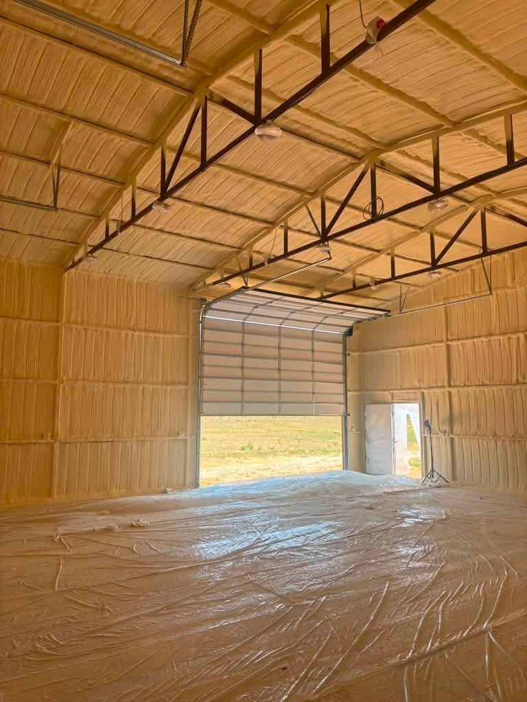 Empty barn interior with straw walls, metal roof trusses, and a large open garage door.