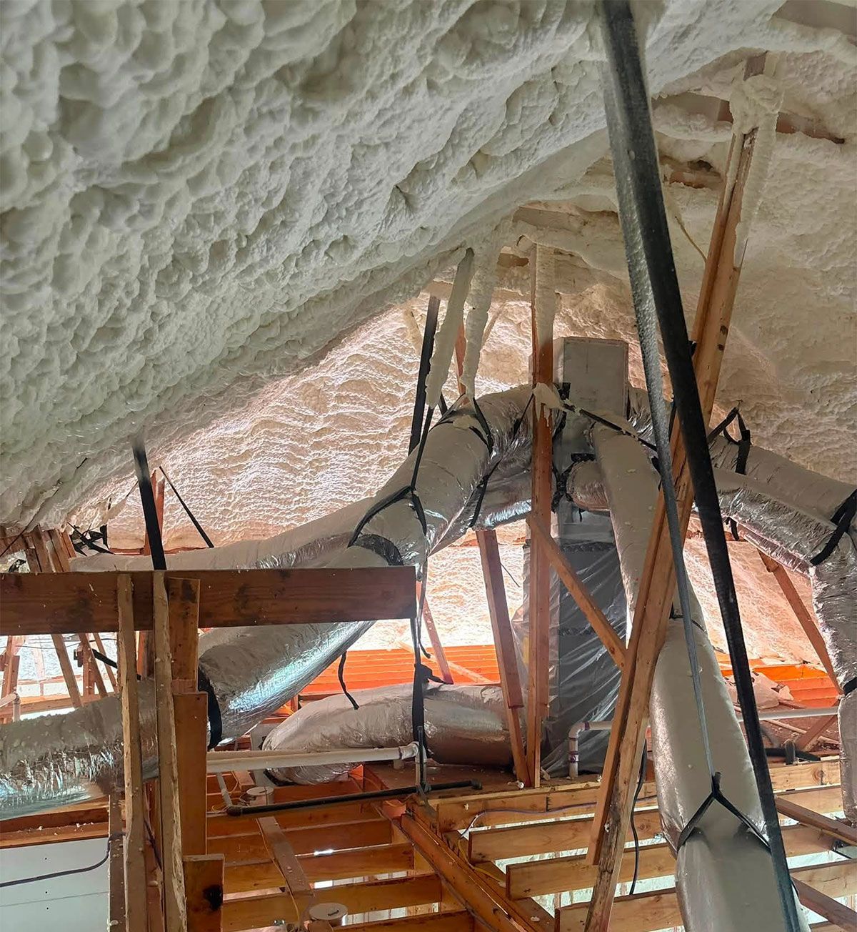 Insulated attic space with exposed wooden beams, ducting, and scaffolding under a sloped roof.
