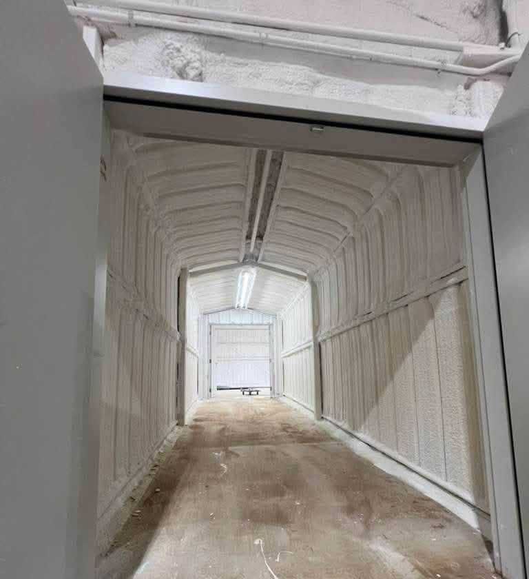 Narrow white industrial tunnel with a dirt floor and a bright opening at the far end