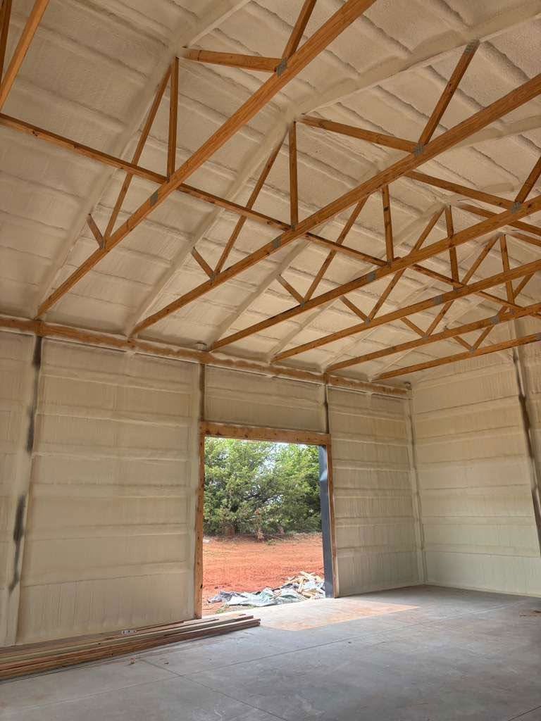 Inside a large unfinished shed with exposed trusses and open doorway to a dirt lot.