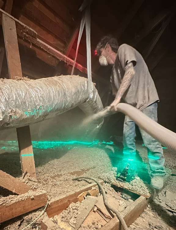 Worker spraying material inside an attic beside a large duct and exposed beams