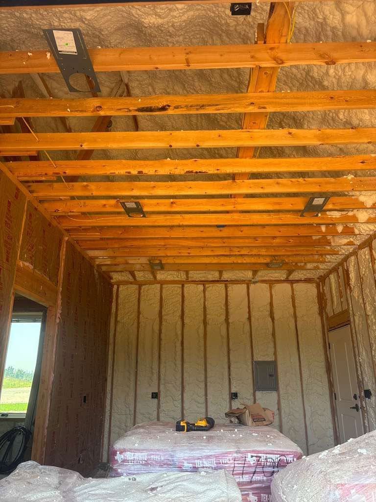 Interior of an unfinished room with exposed wooden ceiling beams and insulated walls, stacks of materials inside