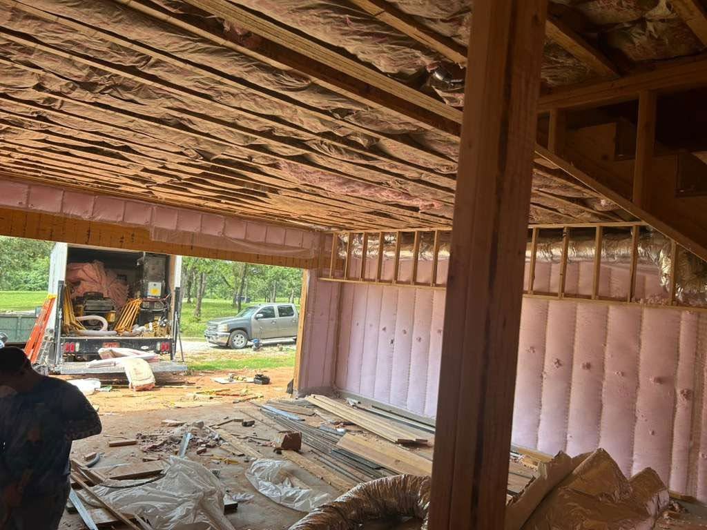 Damaged wooden interior with debris and a partially collapsed roof, opening to a yard outside.
