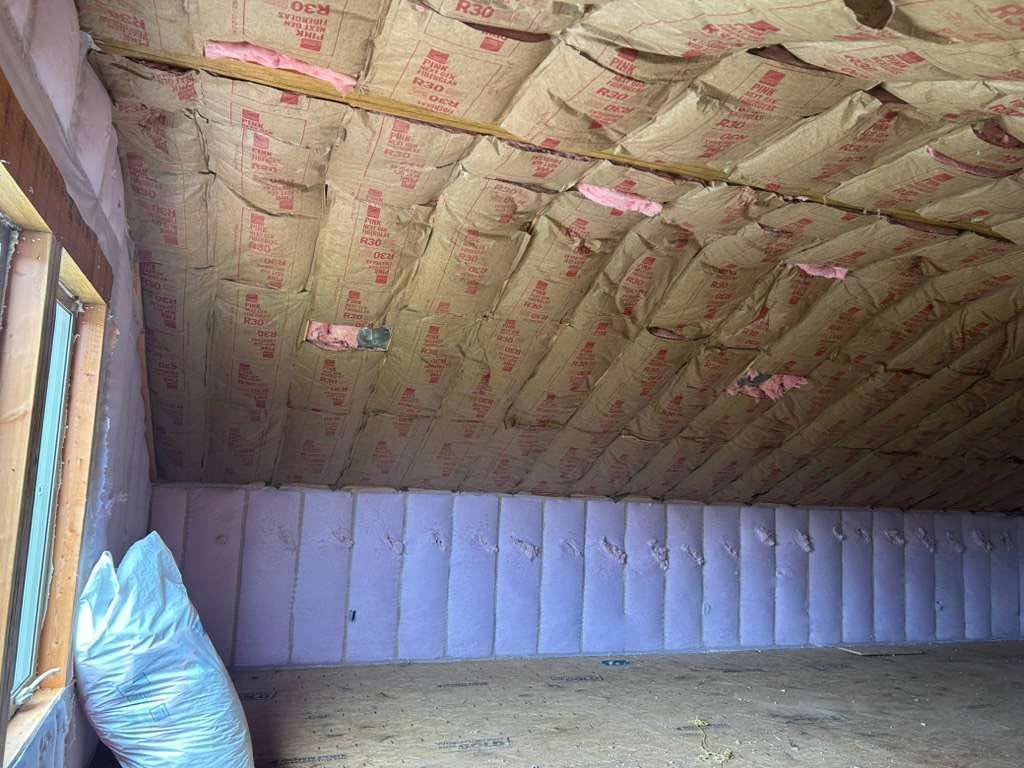 Attic interior with sloped insulated ceiling, exposed wood wall, and a blue pillow in the corner