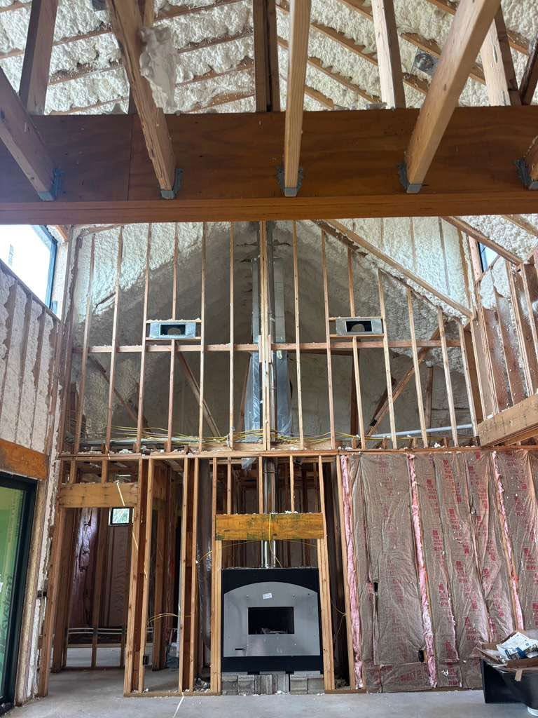 Interior of a house under construction with exposed wooden framing, insulation, and a vaulted ceiling.