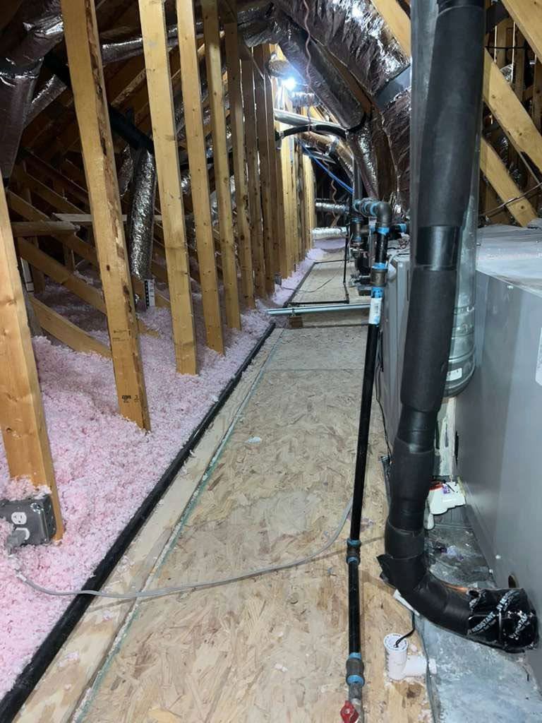 Attic with exposed wooden beams, pink insulation, and black ductwork along a narrow walkway