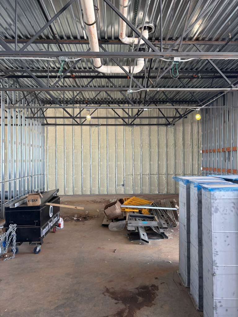 Empty industrial warehouse interior with metal framing, work tables, and stacked blue bins