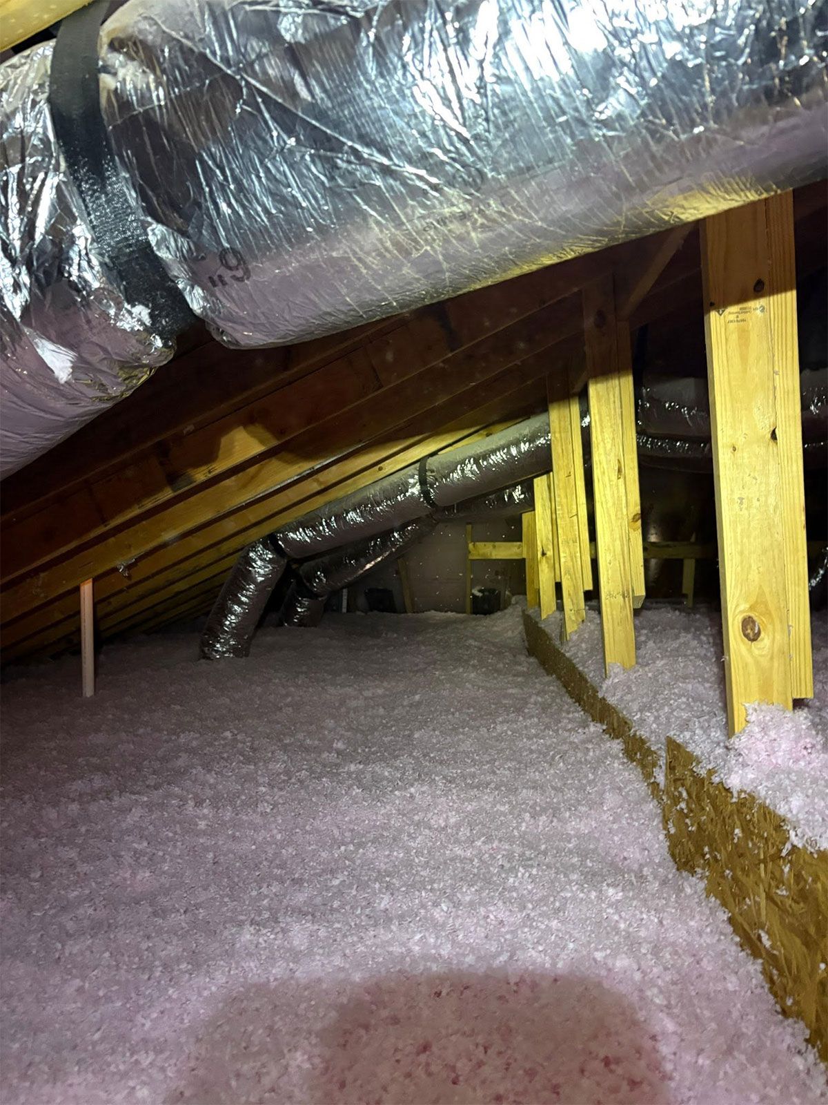 Attic crawlspace with exposed insulation, sloped roof rafters, and wooden support posts.