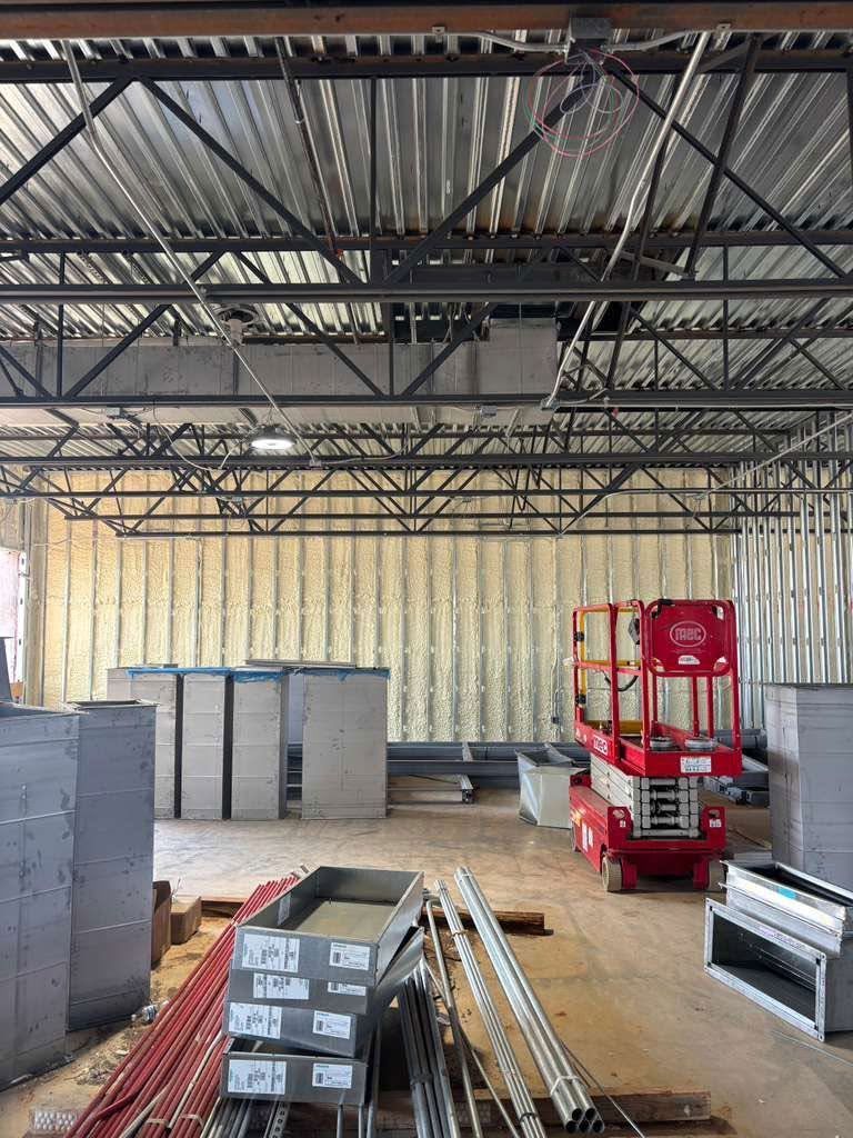 Interior of a warehouse under construction with steel beams, stacked materials, and a red lift