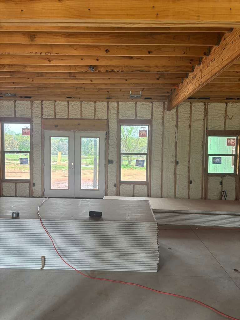 Unfinished room interior with exposed wood ceiling, insulated walls, windows, and a low stacked panel platform.