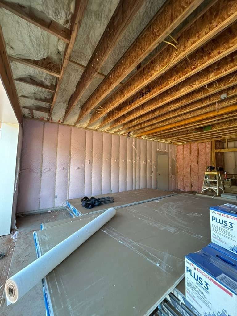 Interior under construction with exposed ceiling beams, insulation, drywall, and rolled flooring materials on the floor