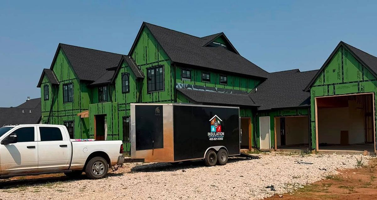 Green house under construction with white pickup truck and trailer in front, on a gravel lot