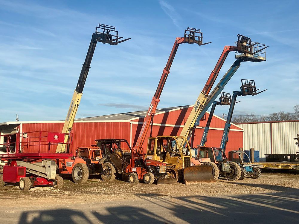 Five colorful telescopic forklifts lined up in a gravel lot beside a red shipping container under a blue sky.