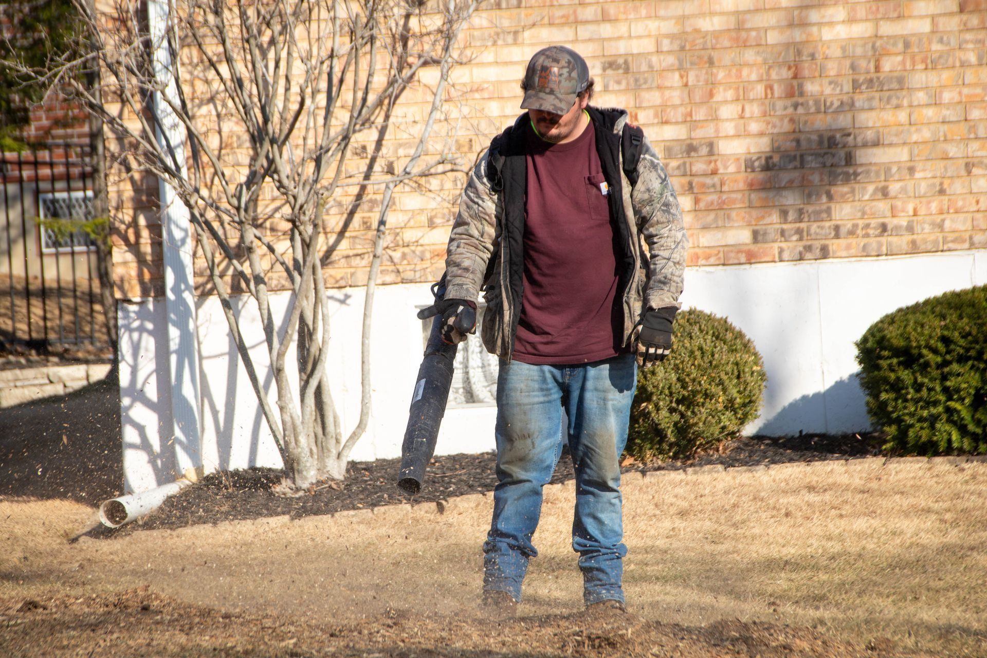 Man using leaf blower on a lawn with a brick building in the background.
