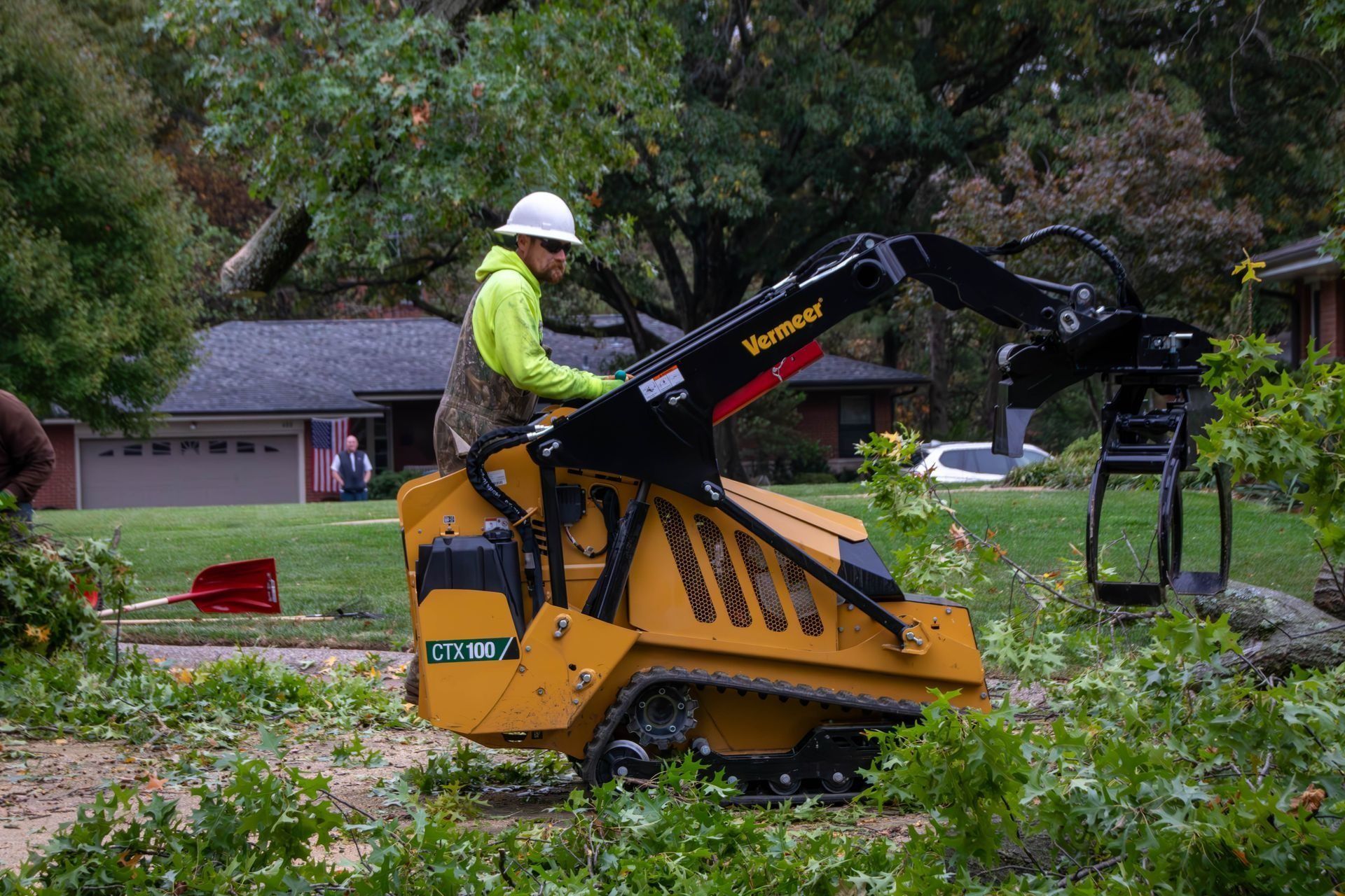 Man in yellow vest operates a yellow stump grinder to clear fallen tree branches.