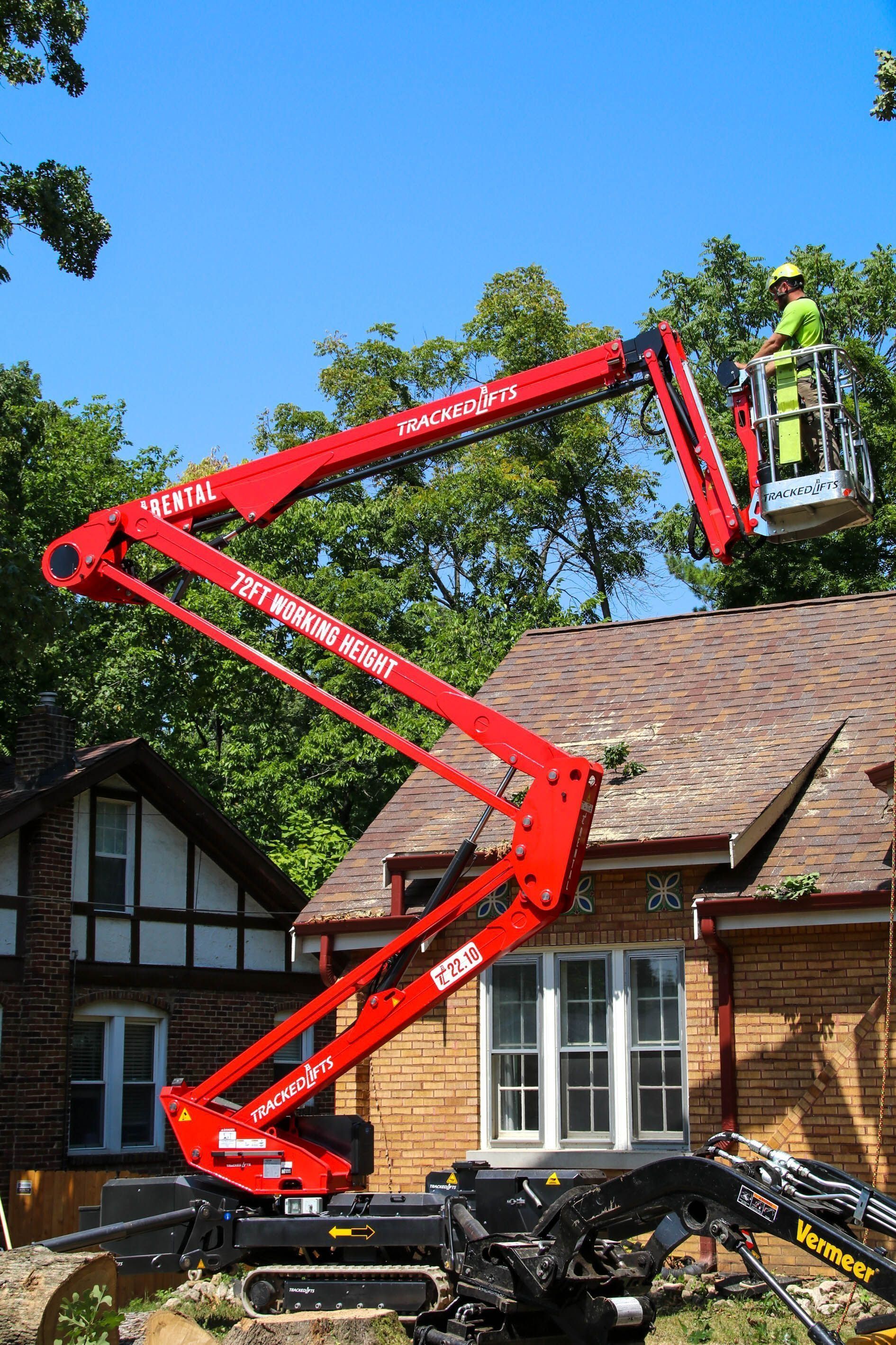 Red articulating boom lift with a worker trimming tree branches near a house.