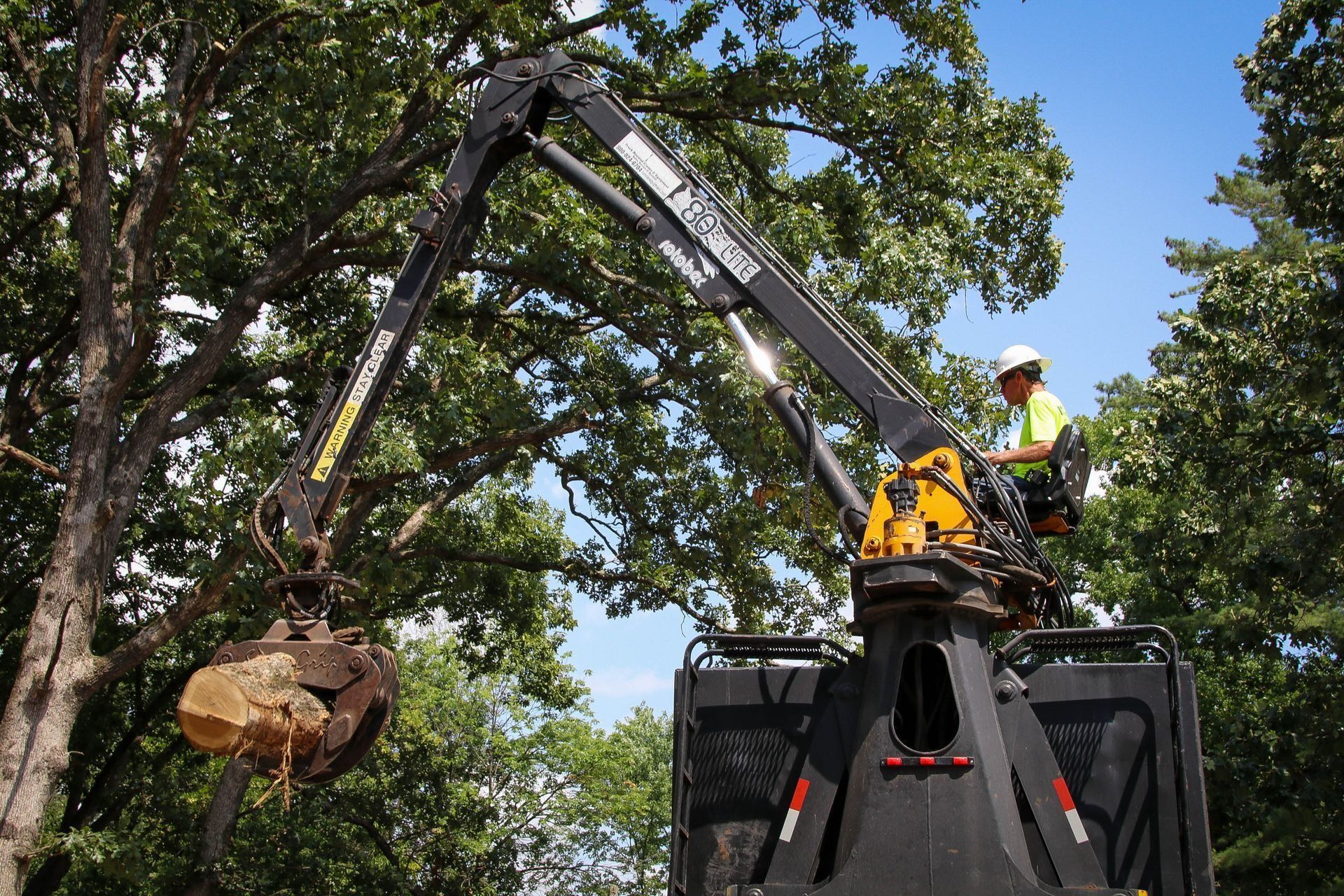 Person in lift operates a crane holding a large rock, trees in background.