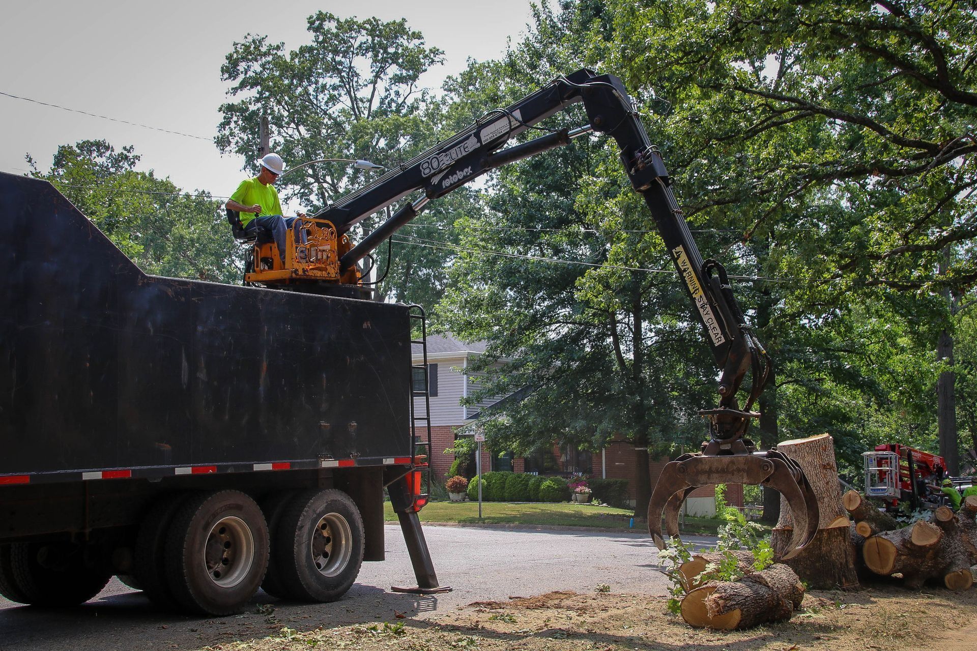 Truck with crane loading logs on a street. Operator in a hard hat, daytime.