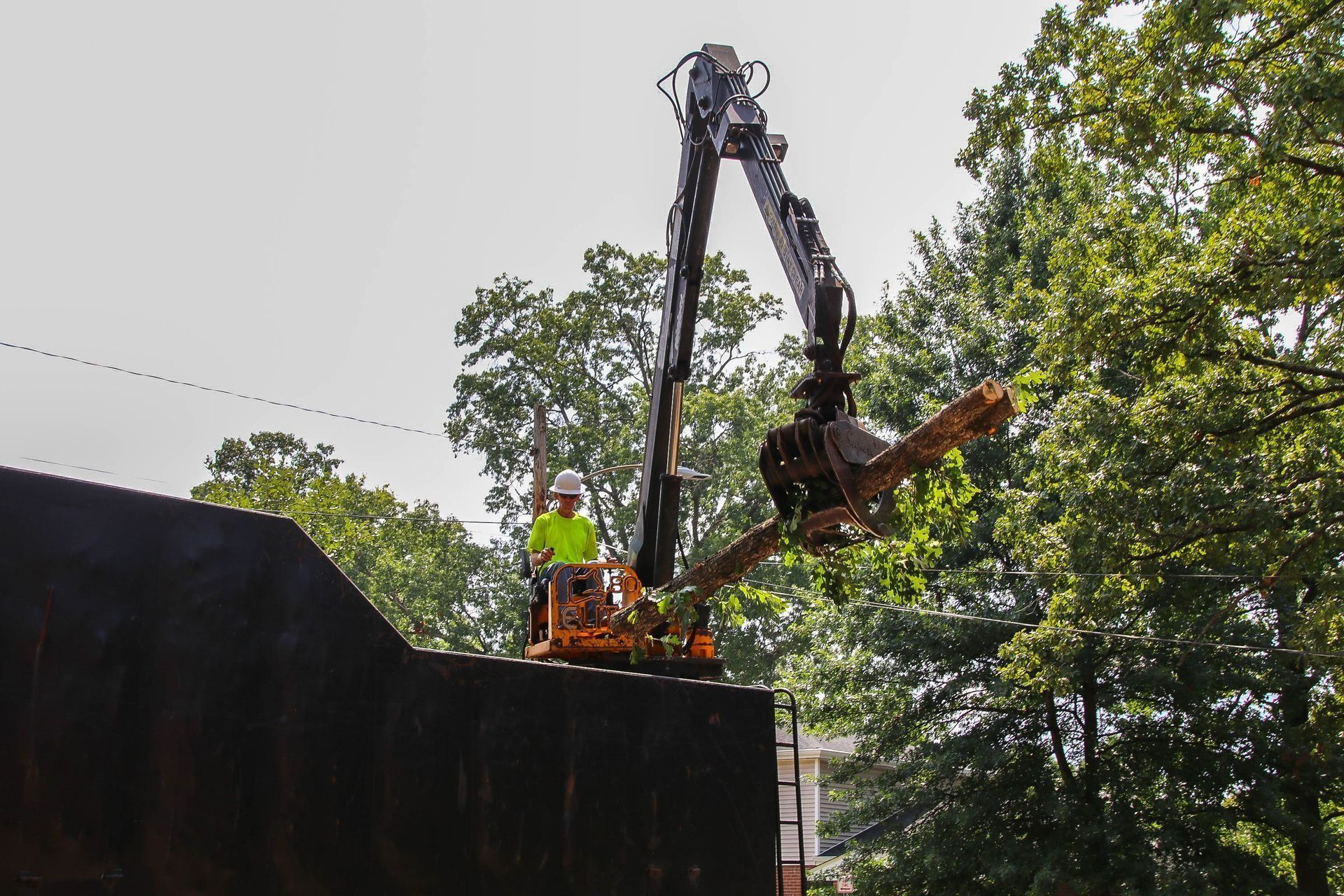 Construction worker in a lift operating an excavator with trees in the background.