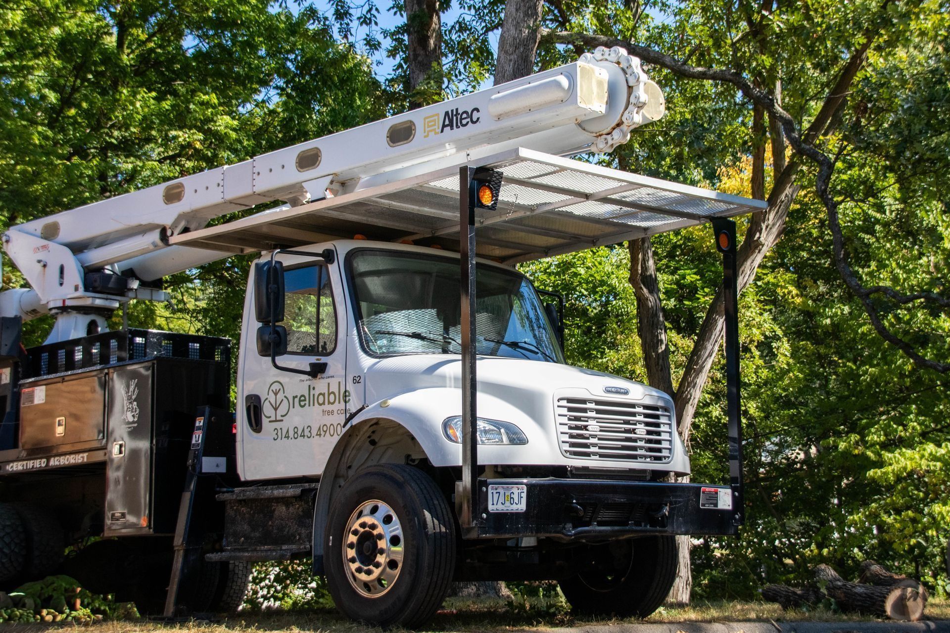 White utility truck with an extended boom and canopy parked by trees.
