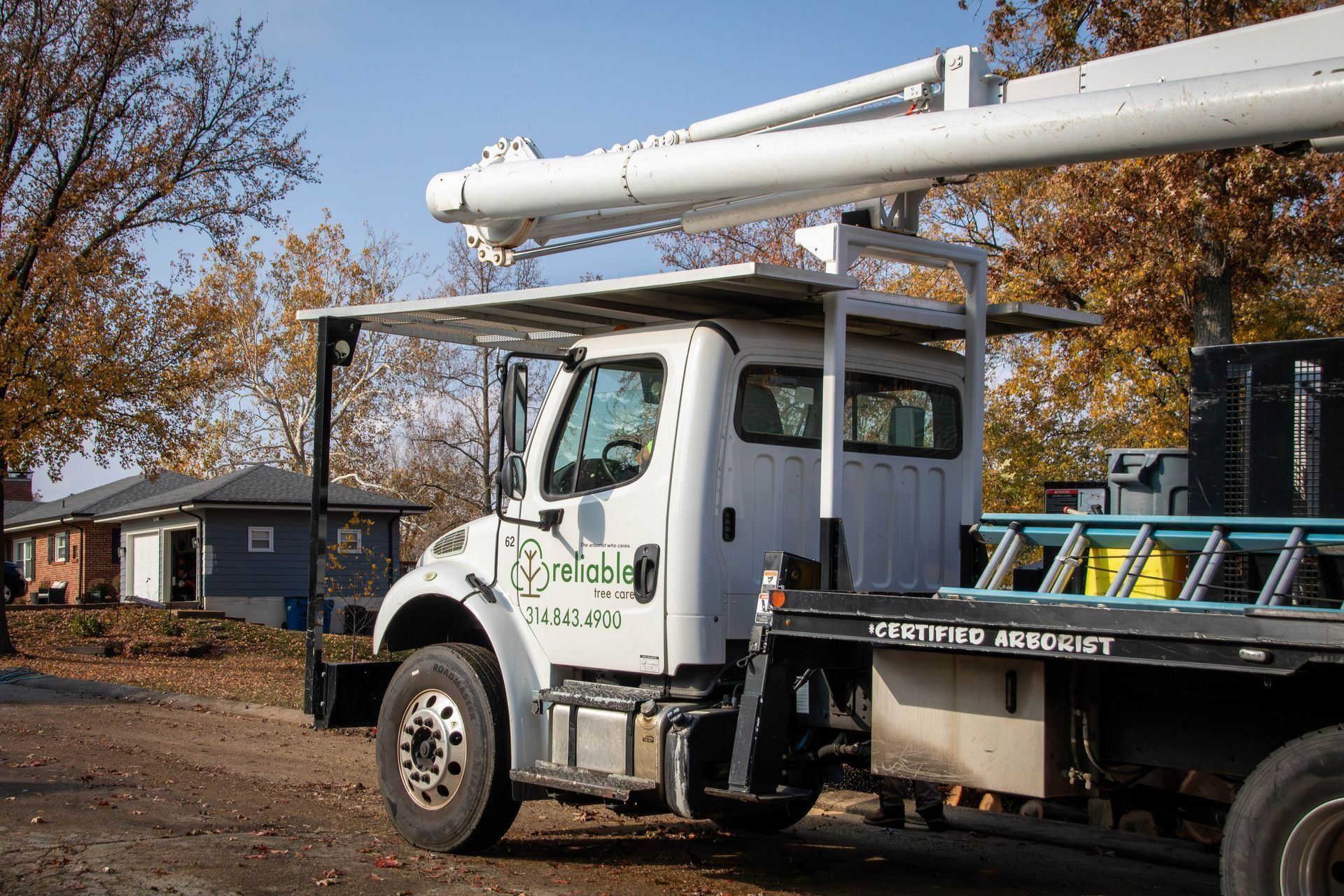 White utility truck with an aerial lift parked on a street with houses in the background.