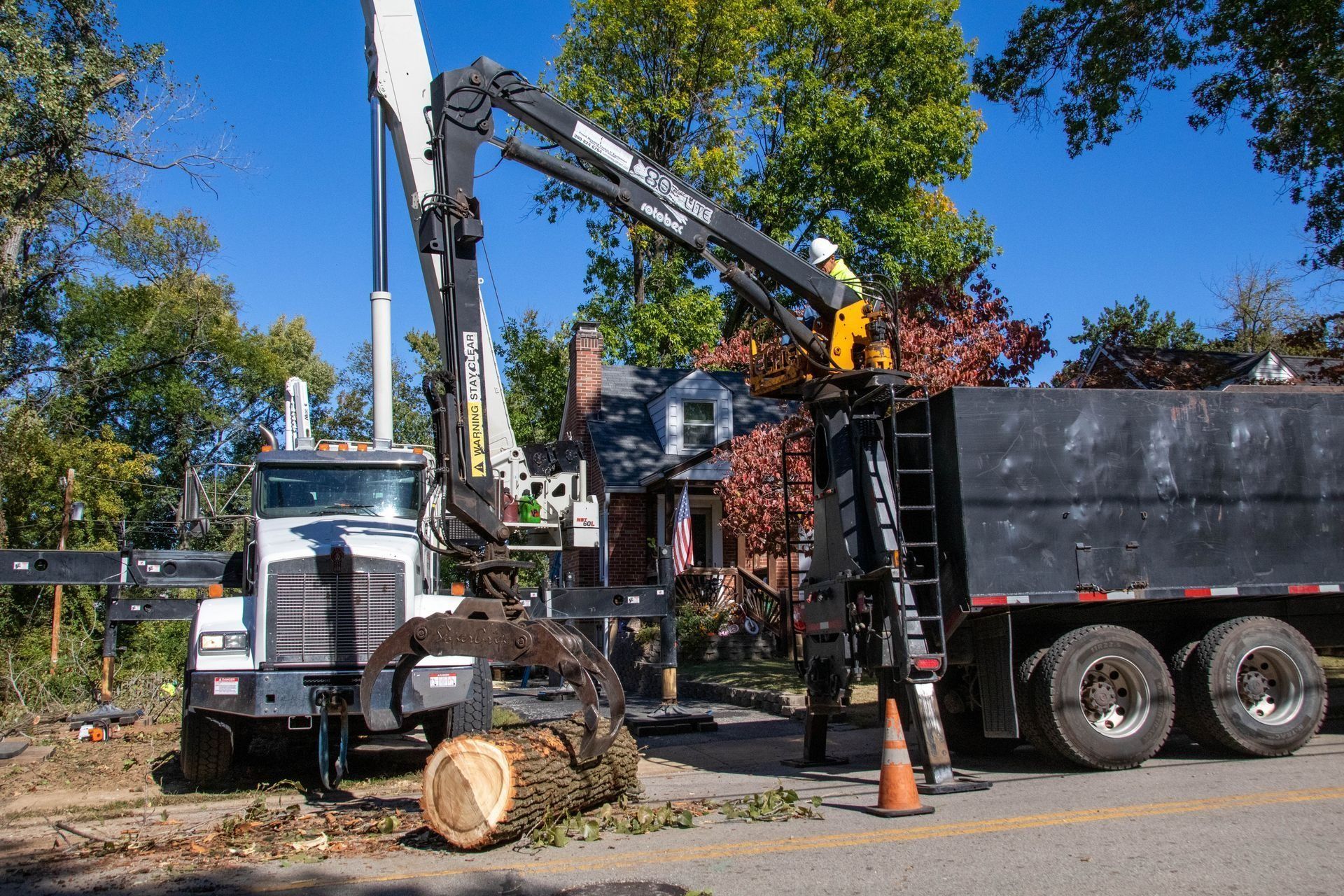 A tree service truck using a crane to lift a tree trunk, removing a fallen tree.