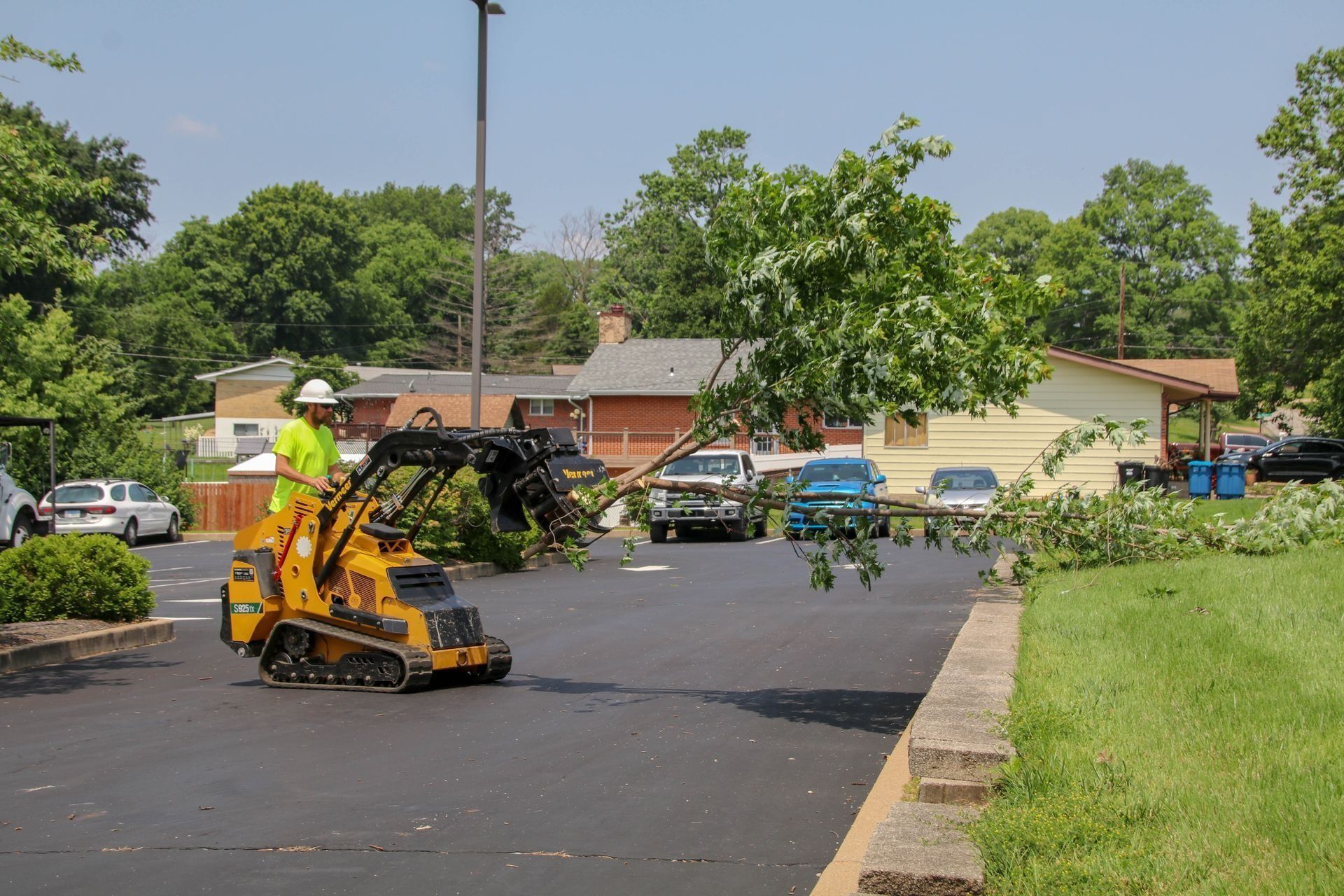 Yellow machine with a person in a safety vest moving tree branches in a parking lot.