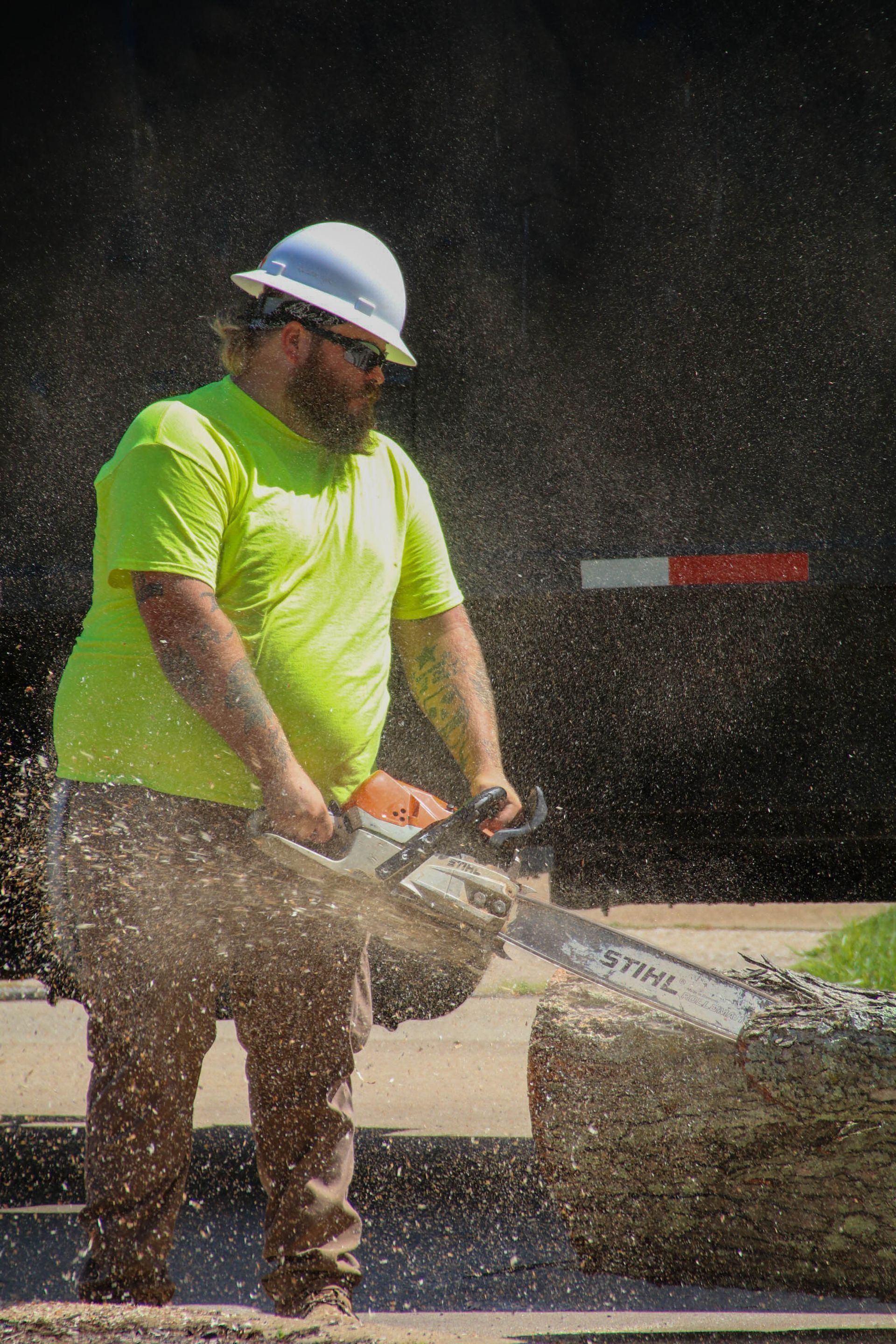 Construction worker in safety gear using a chainsaw on a stone block, sawdust flying.