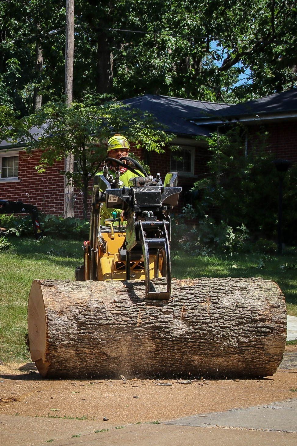 Person operating a lumber saw machine cutting a large log outdoors.