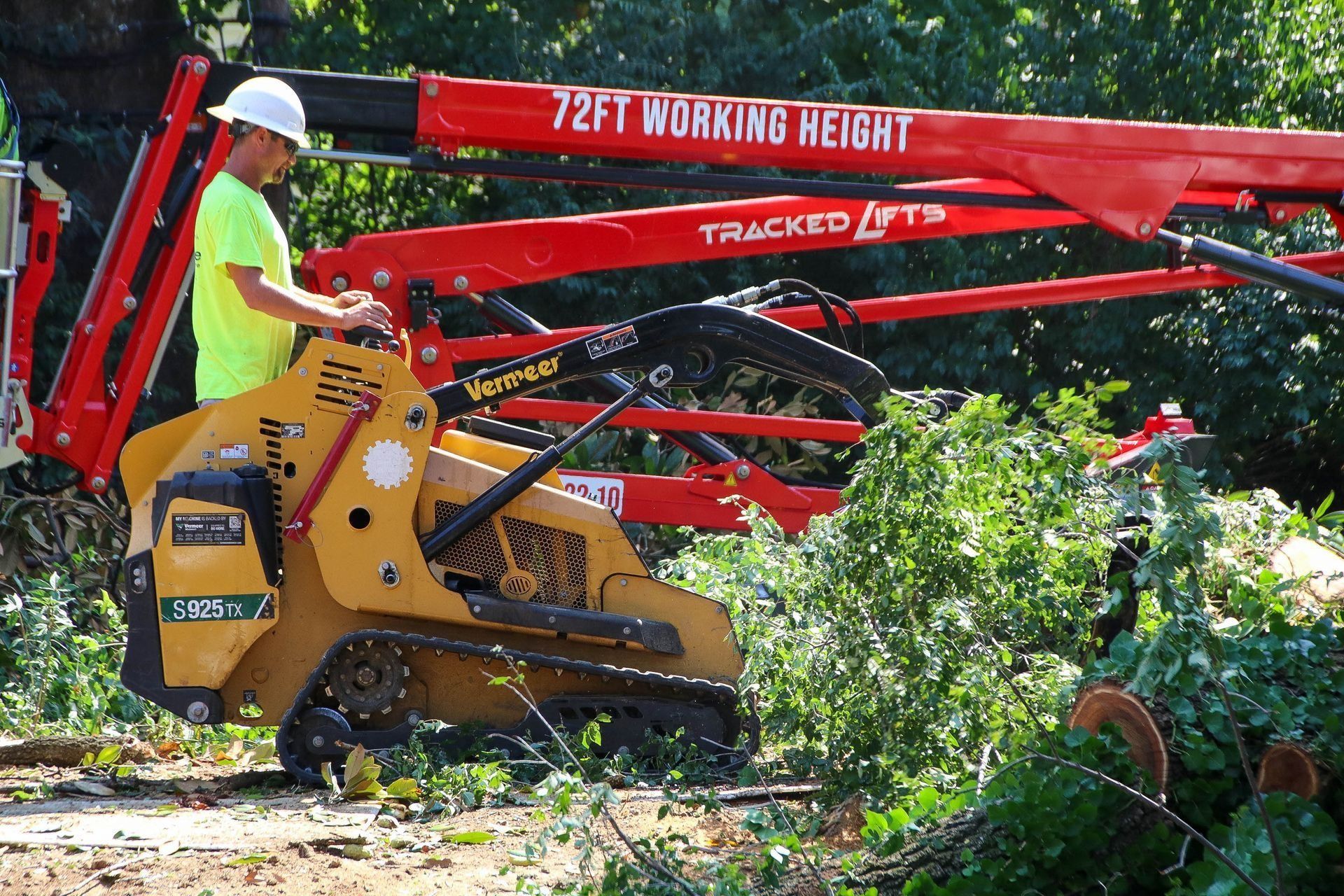 Man operating a tracked lift with a tree stump grinder.  Red lift boom says 