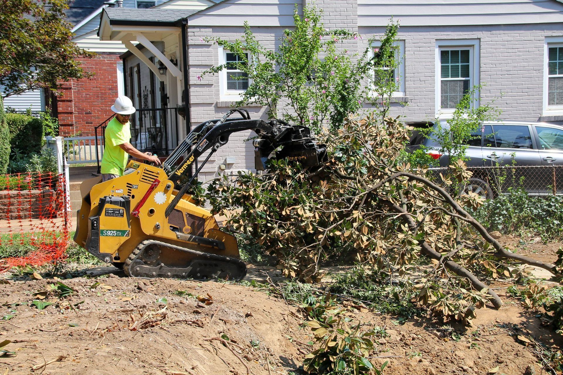 Man operating a small excavator removing tree branches from a construction site.