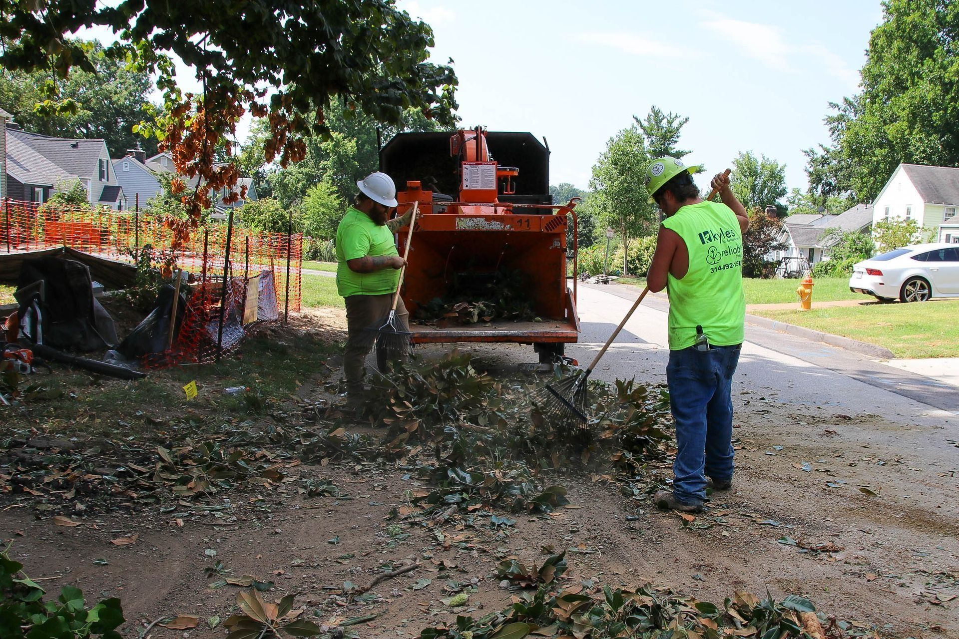 Two workers in neon vests feeding branches into a wood chipper on a residential street.