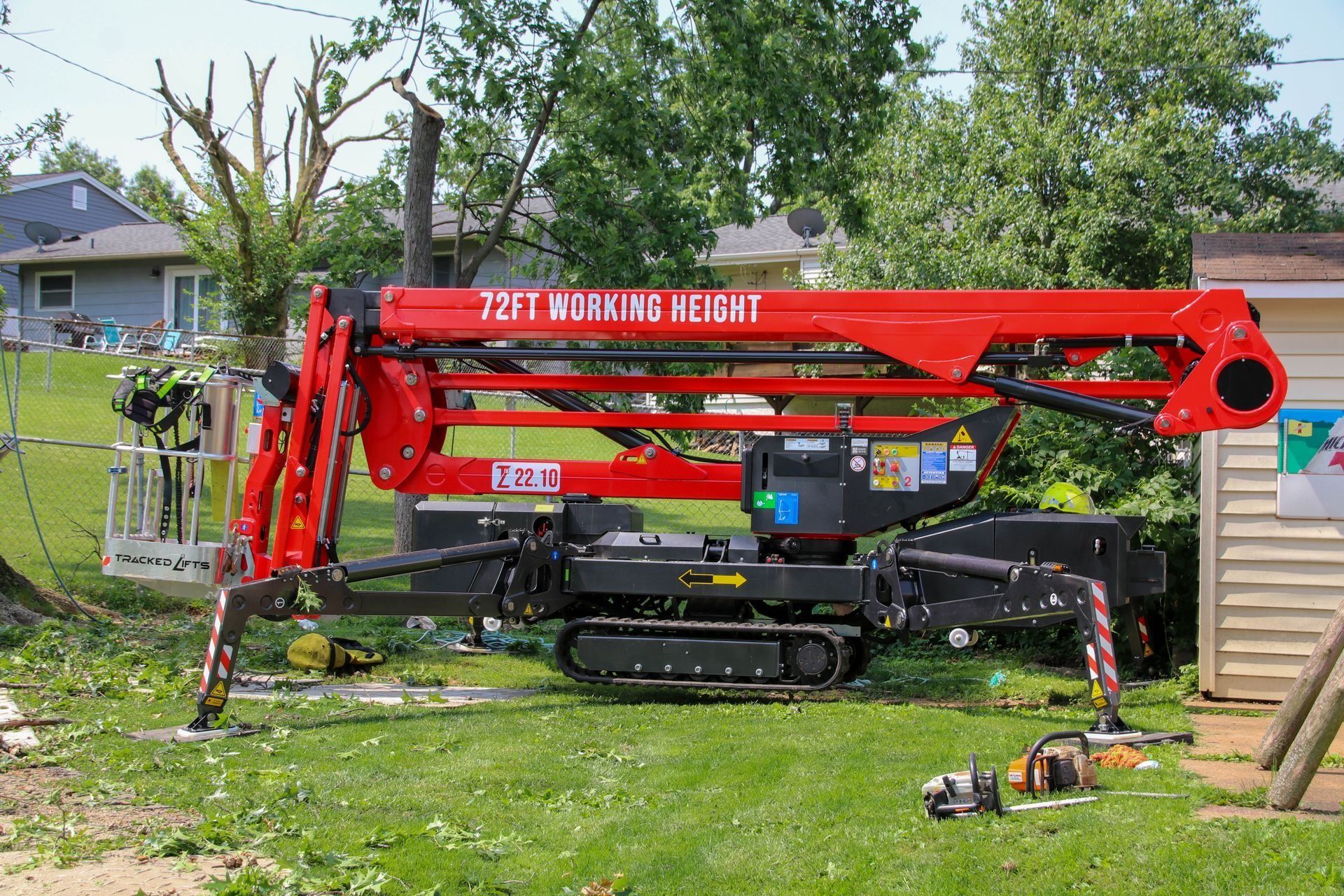 Red and black tracked aerial lift with 72 ft working height, positioned in a yard next to a tree.