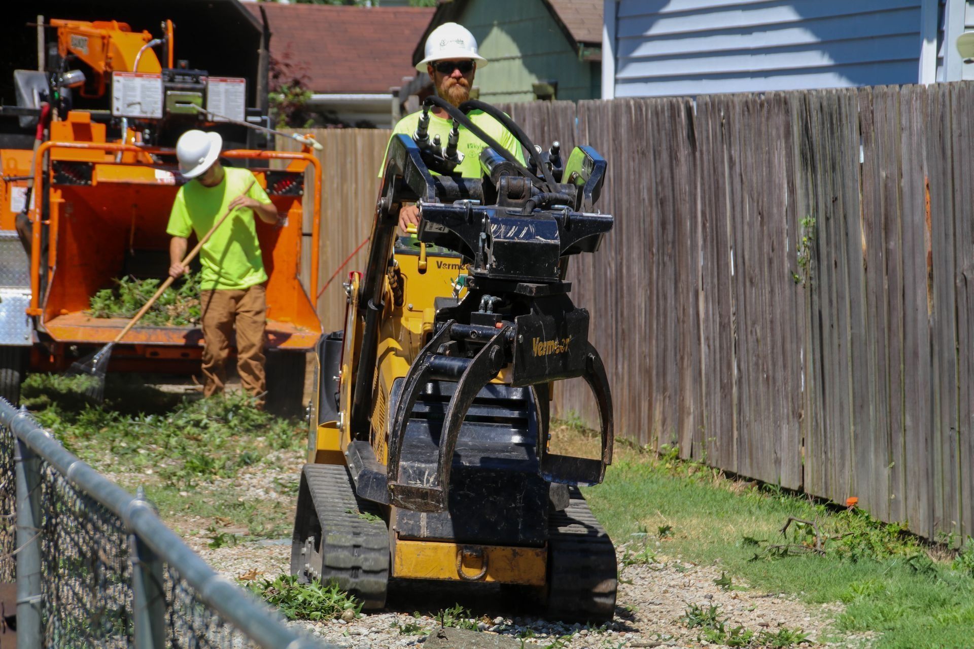 Two workers chipping brush; one in a loader, the other feeding a wood chipper.