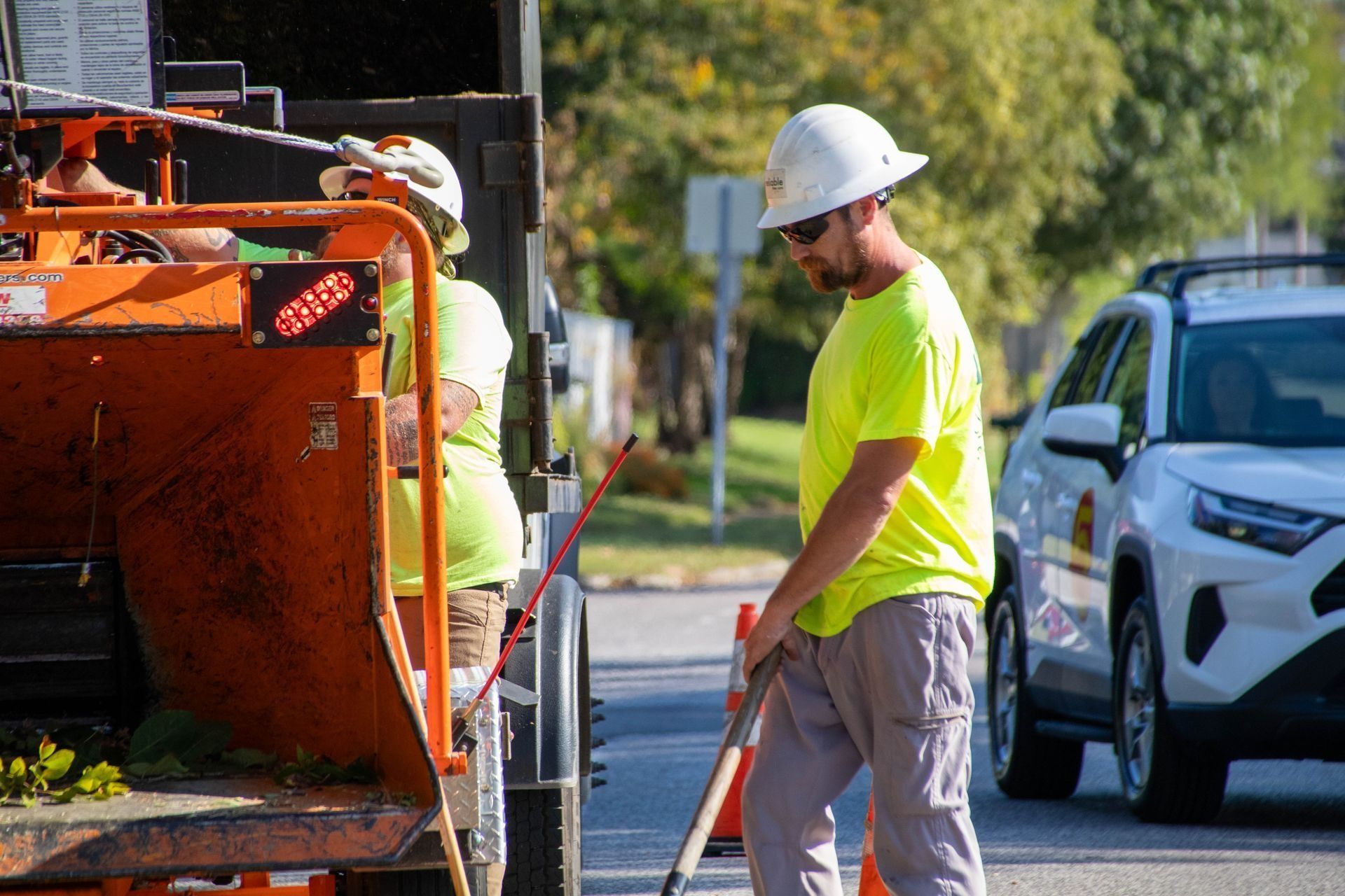 Two workers in safety vests and hard hats operating a wood chipper on a street.