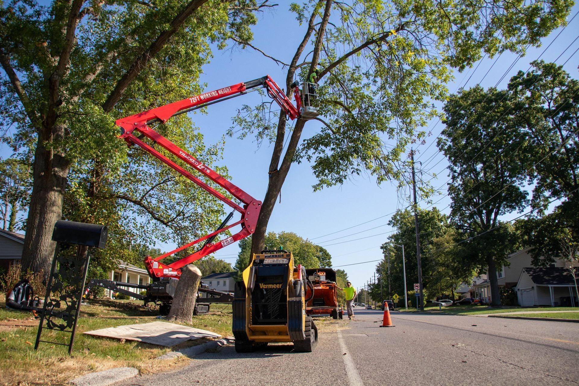 A red tree-trimming lift truck is working on a tree near power lines along a street.