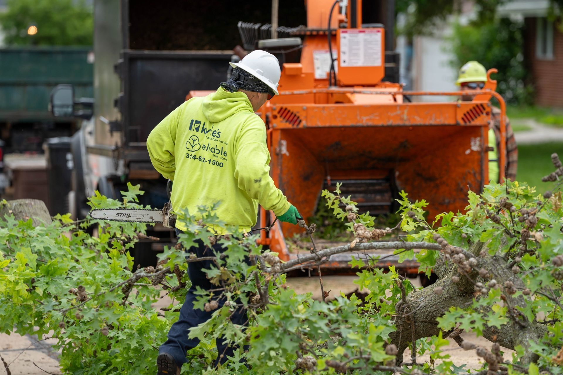 Worker in yellow jacket feeding branches into orange wood chipper.
