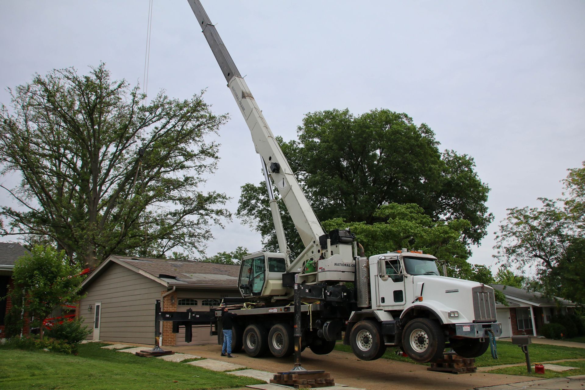 Crane lifting a tree stump from a residential yard with a house in the background.