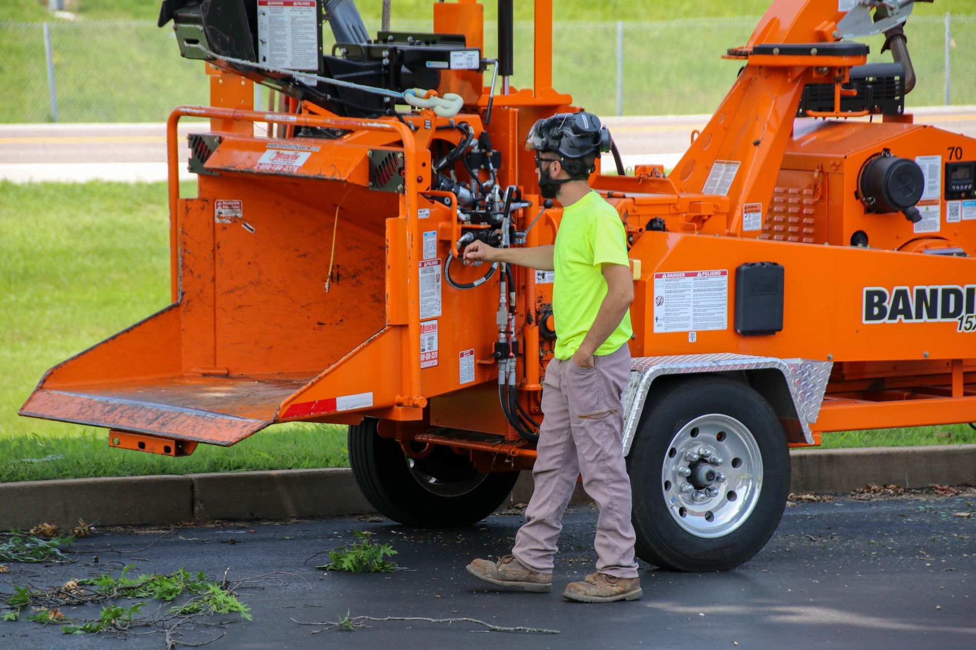 Man operating a bright orange wood chipper; outdoor setting with green foliage.