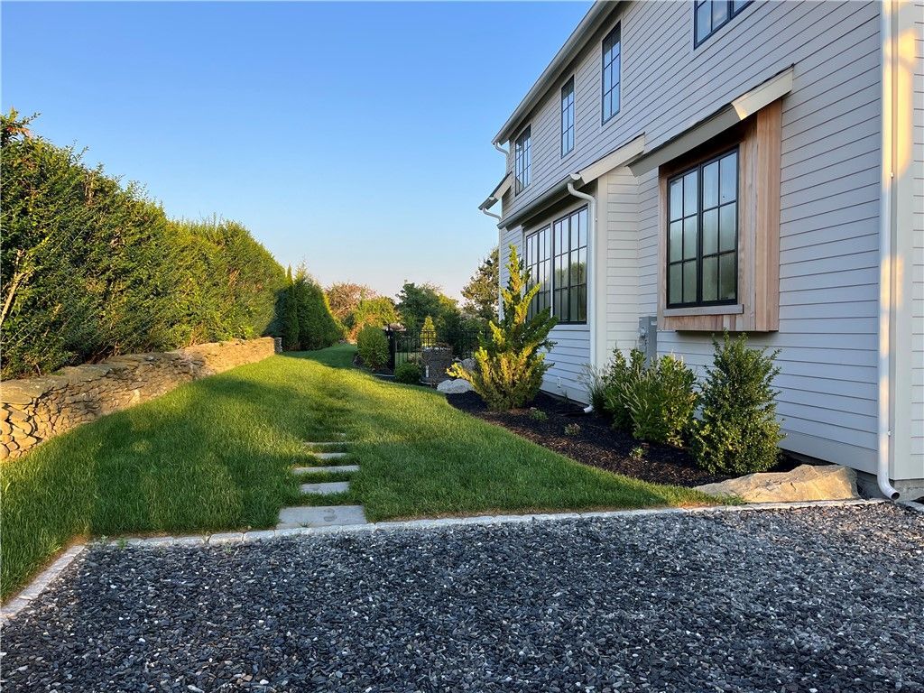 Side view of a white house with a landscaped yard and a gravel driveway.