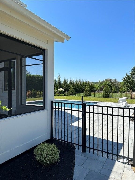 A sunny outdoor scene featuring a pool behind a black fence, seen from a white building with large windows.