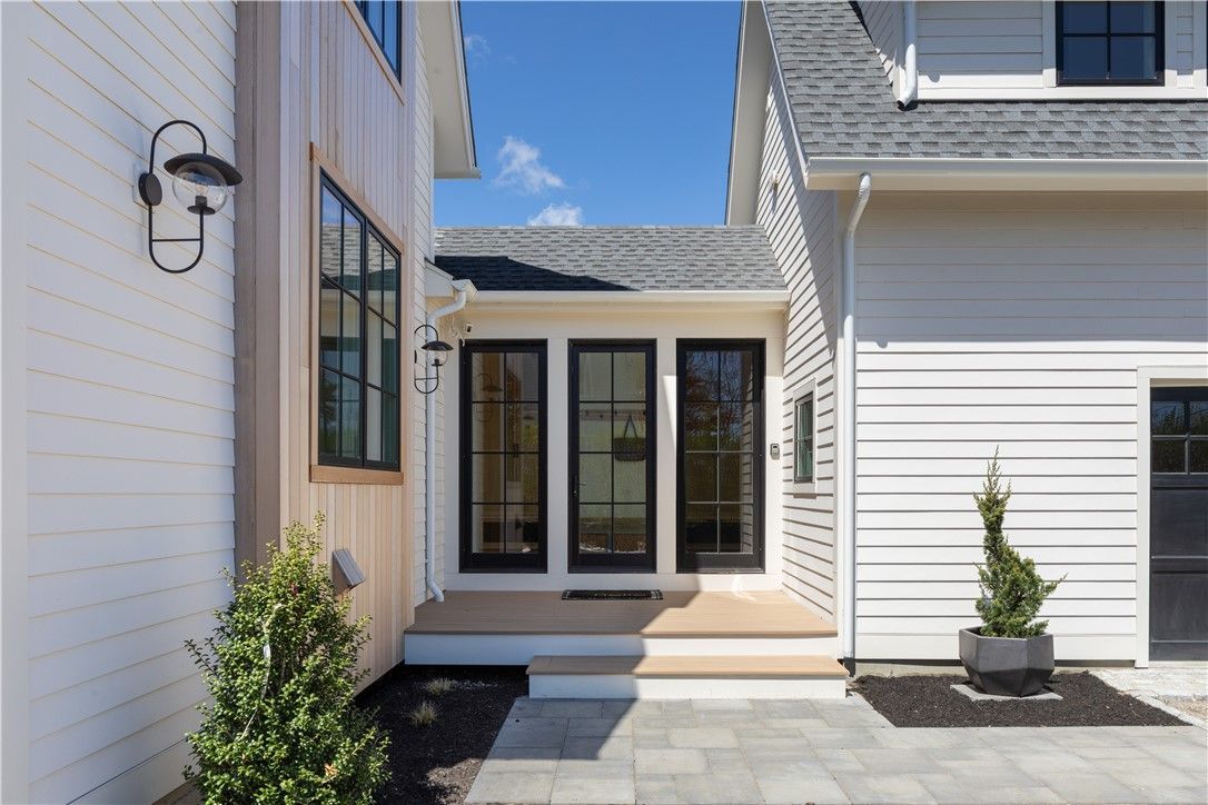 Exterior of a white house with black-framed doors, small porch, and paving. Sunny day, blue sky.